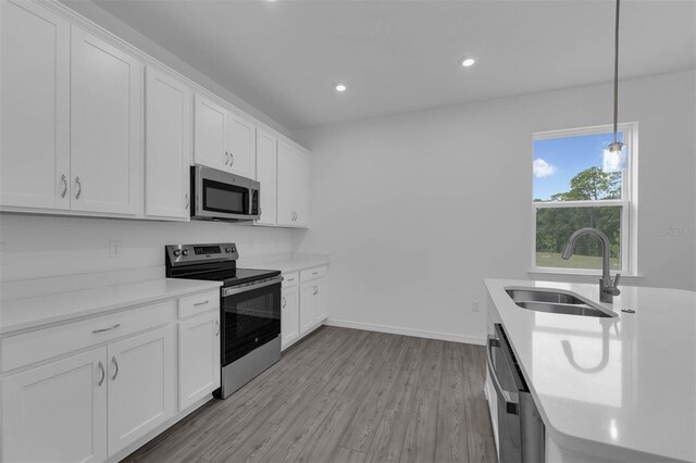 kitchen with stainless steel appliances, light countertops, a sink, light wood-style flooring, and white cabinetry