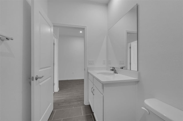 half bath with baseboards, toilet, vanity, and tile patterned floors