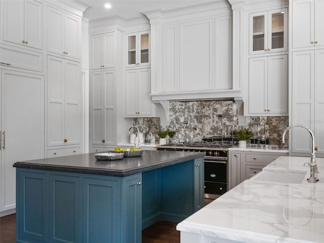 kitchen featuring range with gas stovetop, a sink, glass insert cabinets, a center island with sink, and white cabinetry