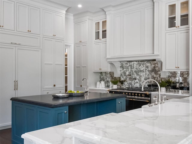 kitchen with white cabinets, double oven range, decorative backsplash, glass insert cabinets, and an island with sink