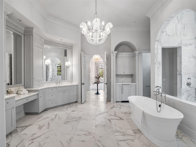 full bathroom featuring marble finish floor, vanity, crown molding, a soaking tub, and a notable chandelier