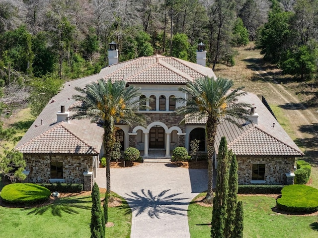 view of front of property featuring a chimney, stone siding, and a tiled roof