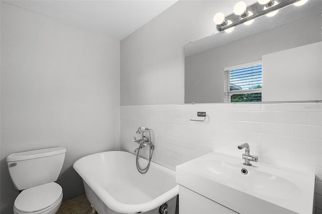 full bathroom with a freestanding tub, vanity, toilet, and tile walls