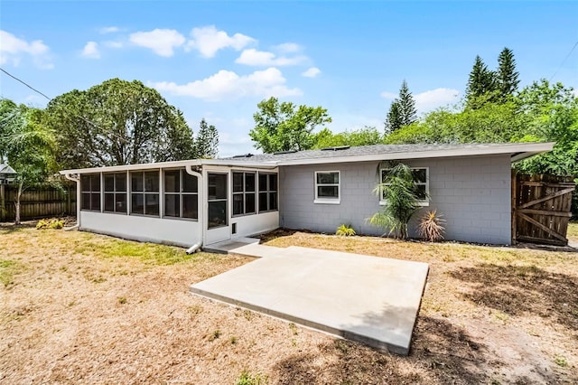 rear view of property featuring a sunroom, fence, a yard, a patio, and concrete block siding