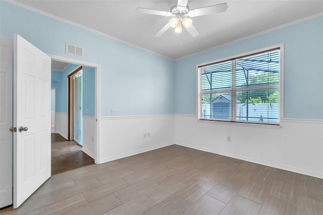 spare room featuring ceiling fan, baseboards, wood finished floors, visible vents, and ornamental molding
