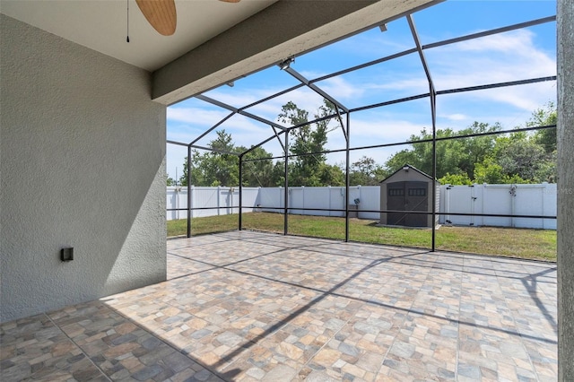 view of patio with ceiling fan, glass enclosure, an outdoor structure, a shed, and a fenced backyard