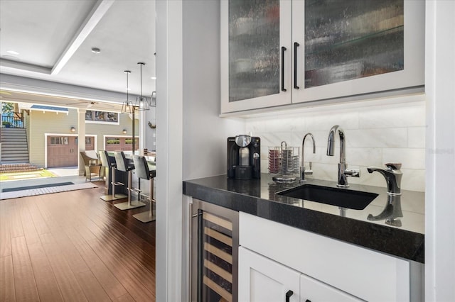 bar featuring tasteful backsplash, a sink, hanging light fixtures, beverage cooler, and dark wood-type flooring