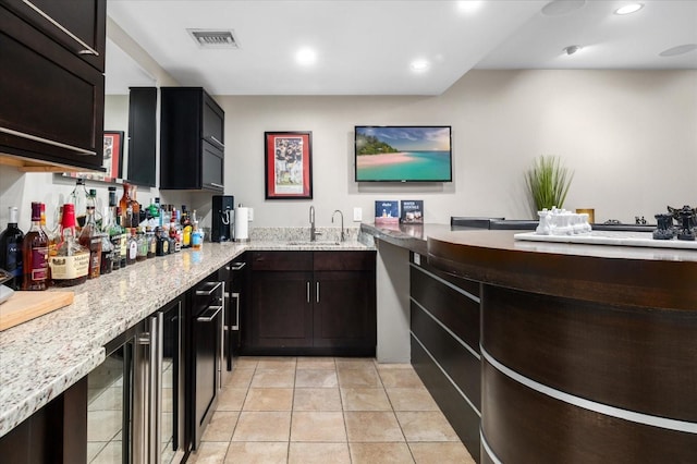 interior space with a sink, light tile patterned flooring, beverage cooler, light stone countertops, and visible vents