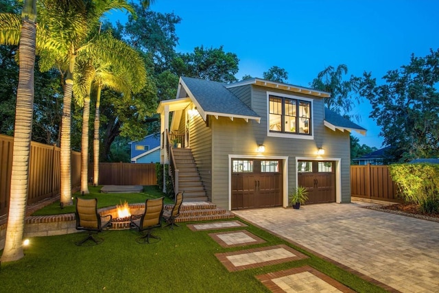 view of front facade with stairway, decorative driveway, a fire pit, a garage, and roof with shingles