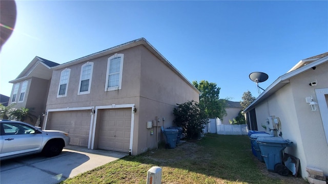view of side of property featuring a garage, concrete driveway, a yard, and stucco siding