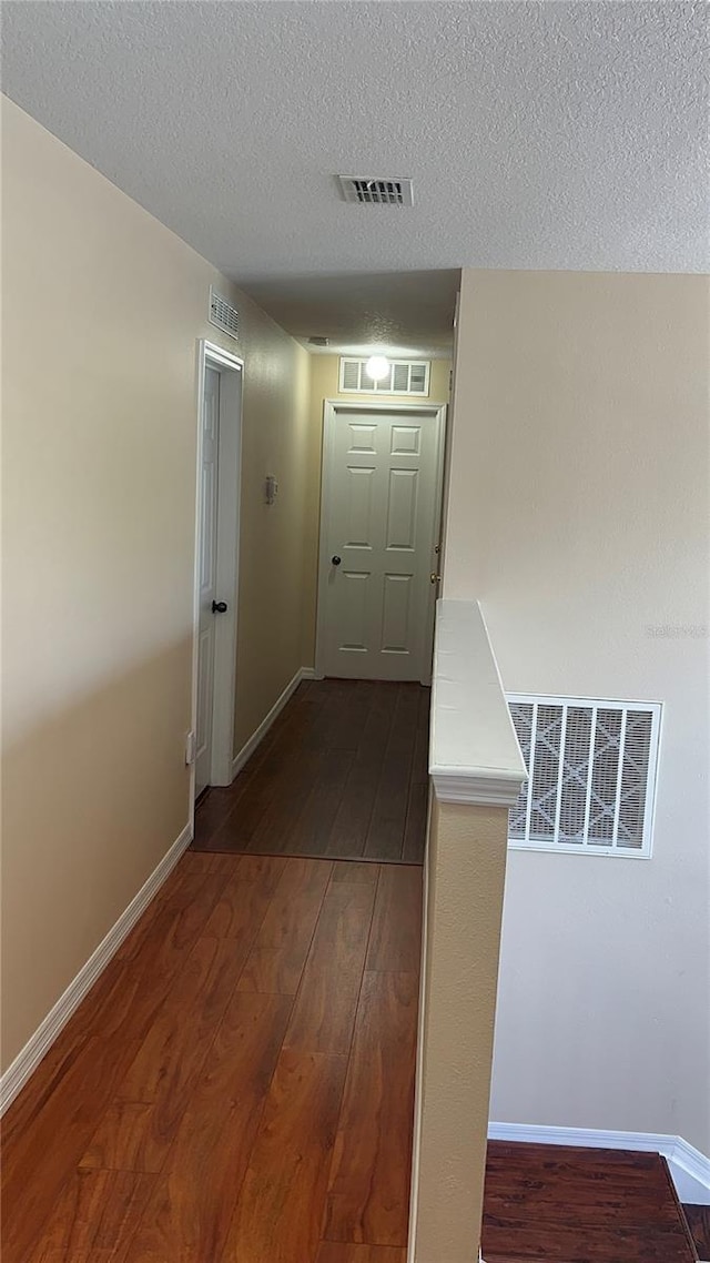 interior space featuring a textured ceiling, baseboards, dark wood-style flooring, and visible vents