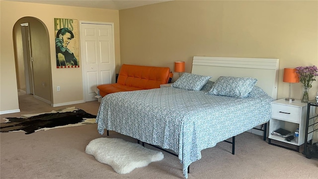 bedroom featuring baseboards, arched walkways, a closet, and carpet