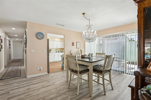 dining room with a textured ceiling, light wood-type flooring, an inviting chandelier, baseboards, and visible vents