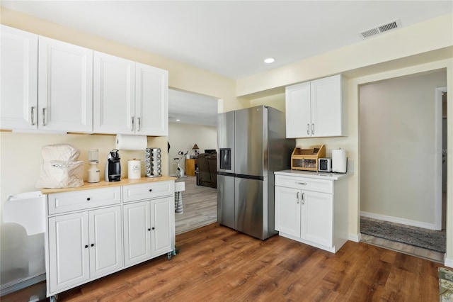 kitchen with wood finished floors, light countertops, white cabinets, stainless steel refrigerator with ice dispenser, and visible vents