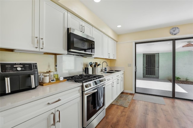 kitchen with light countertops, wood finished floors, a sink, appliances with stainless steel finishes, and white cabinetry