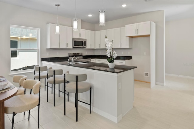 kitchen featuring dark countertops, hanging light fixtures, appliances with stainless steel finishes, and white cabinetry