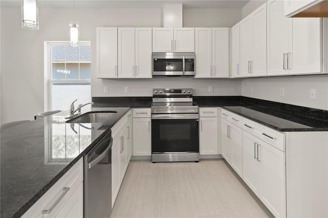 kitchen with appliances with stainless steel finishes, dark stone countertops, a sink, and white cabinetry