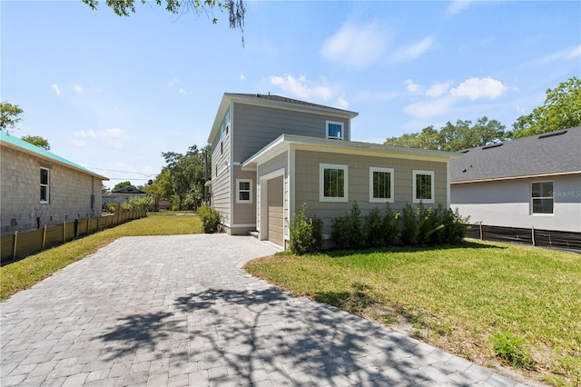 view of front of house with fence, an attached garage, a front lawn, and decorative driveway