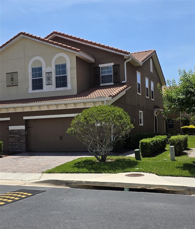 mediterranean / spanish-style home featuring a tiled roof, an attached garage, stucco siding, and decorative driveway