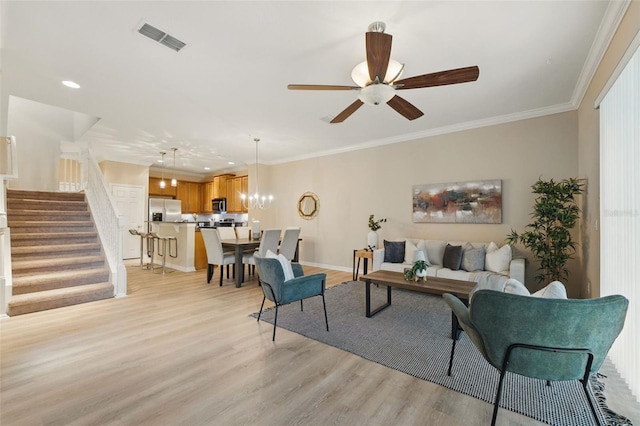 living area featuring visible vents, ornamental molding, stairs, light wood-type flooring, and ceiling fan with notable chandelier