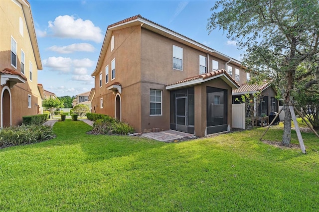 back of property featuring a sunroom, a yard, stucco siding, and a tiled roof