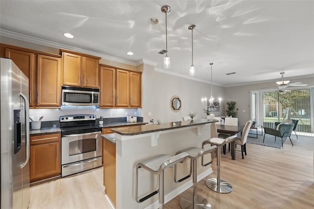 kitchen with brown cabinetry, a breakfast bar area, appliances with stainless steel finishes, ornamental molding, and light wood-style flooring
