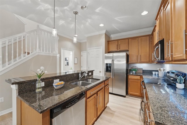 kitchen featuring brown cabinetry, crown molding, dark stone counters, a sink, and appliances with stainless steel finishes