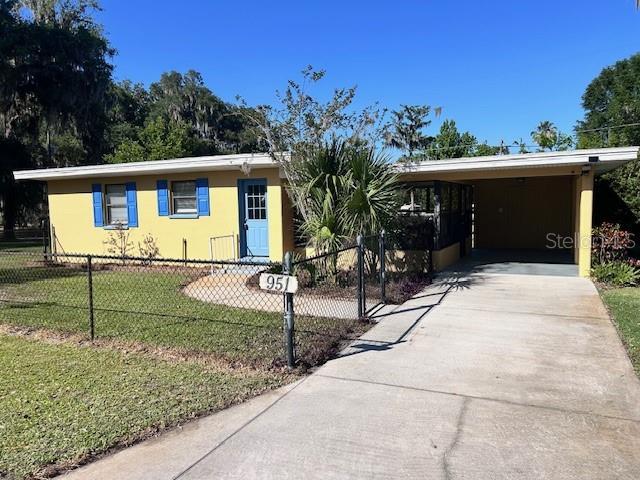 ranch-style home featuring a fenced front yard, a front lawn, driveway, a carport, and stucco siding