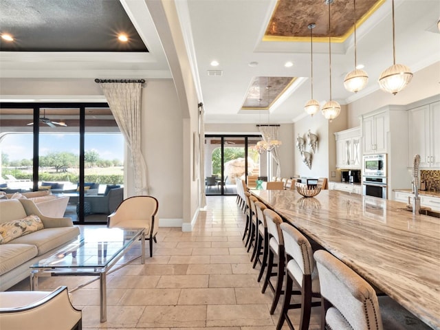 971 Golden Bear Dr, Reunion, FL 34747 - kitchen featuring light stone counters, a breakfast bar area, stainless steel appliances, a tray ceiling, and ornamental molding