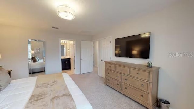 bedroom with ensuite bathroom, visible vents, and light colored carpet