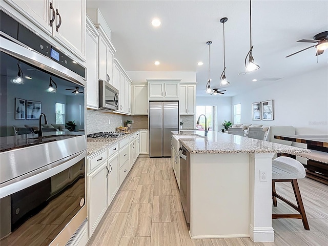 kitchen featuring a sink, decorative backsplash, a ceiling fan, appliances with stainless steel finishes, and open floor plan
