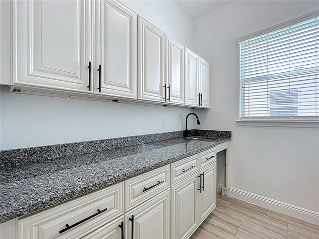 interior space with dark stone counters, a sink, white cabinetry, and baseboards