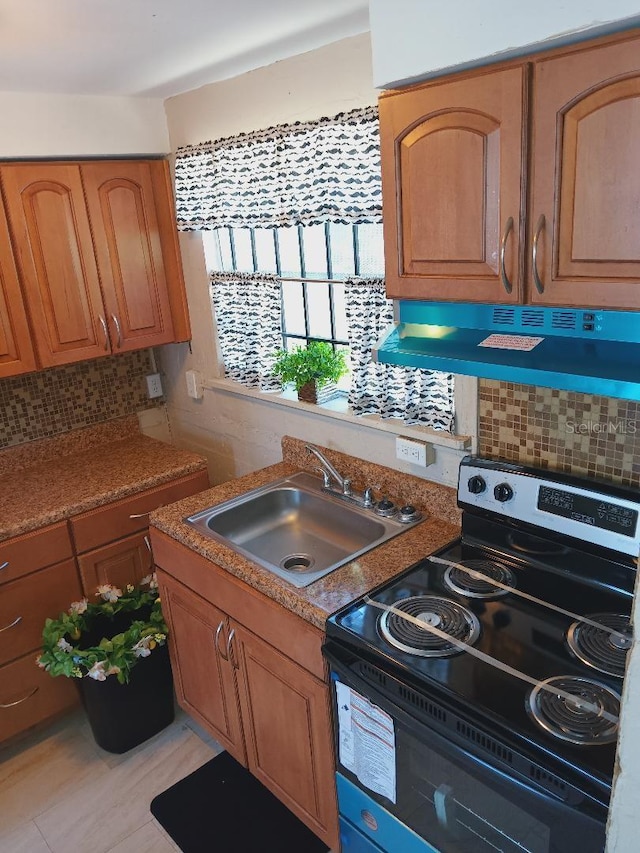 kitchen featuring a sink, stainless steel electric range, decorative backsplash, brown cabinets, and under cabinet range hood