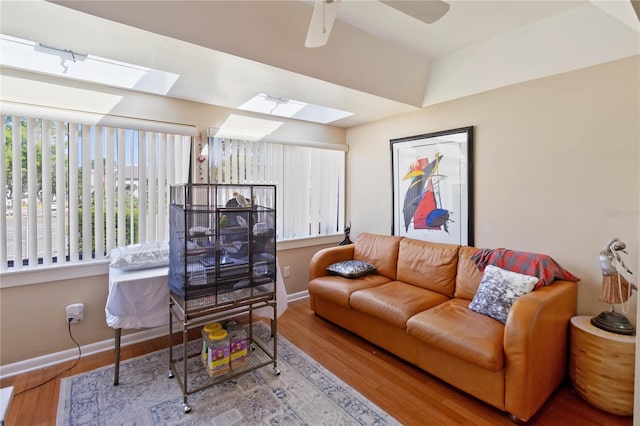 living room with baseboards, a ceiling fan, wood finished floors, and a skylight