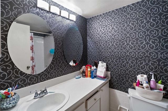 full bath with vanity, tile walls, a shower with shower curtain, wallpapered walls, and a wainscoted wall