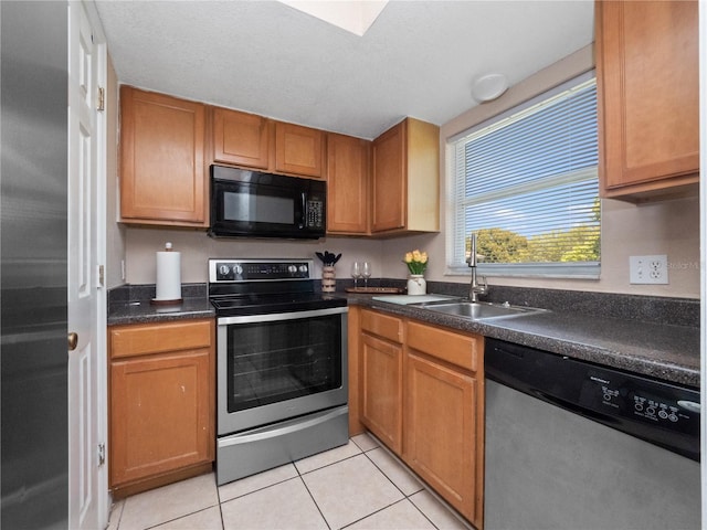 kitchen with dark countertops, a sink, brown cabinets, light tile patterned floors, and stainless steel appliances