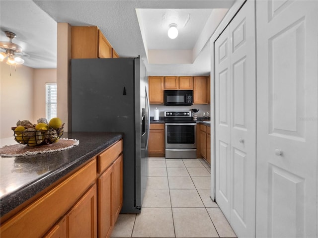 kitchen with a ceiling fan, brown cabinets, light tile patterned flooring, a tray ceiling, and appliances with stainless steel finishes