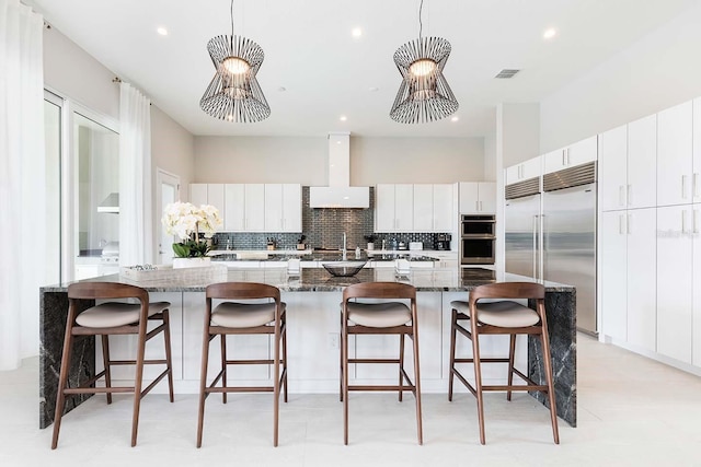 kitchen with range hood, a large island with sink, appliances with stainless steel finishes, backsplash, and white cabinetry