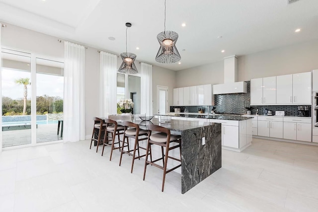 kitchen featuring recessed lighting, white cabinets, a large island, wall chimney exhaust hood, and decorative backsplash