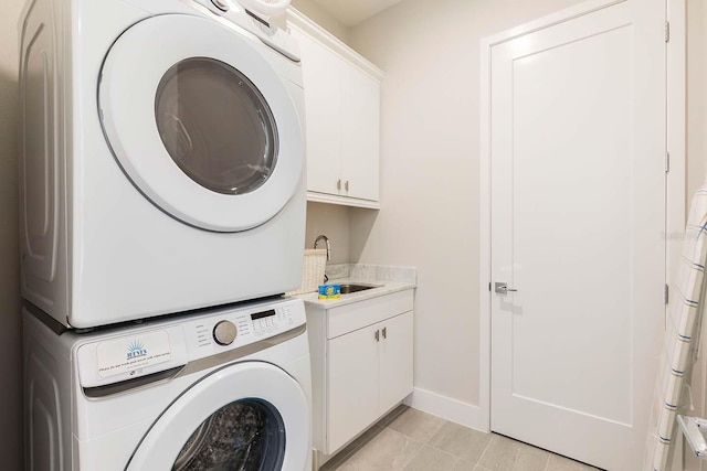 laundry area with stacked washer and dryer, a sink, baseboards, cabinet space, and light tile patterned floors