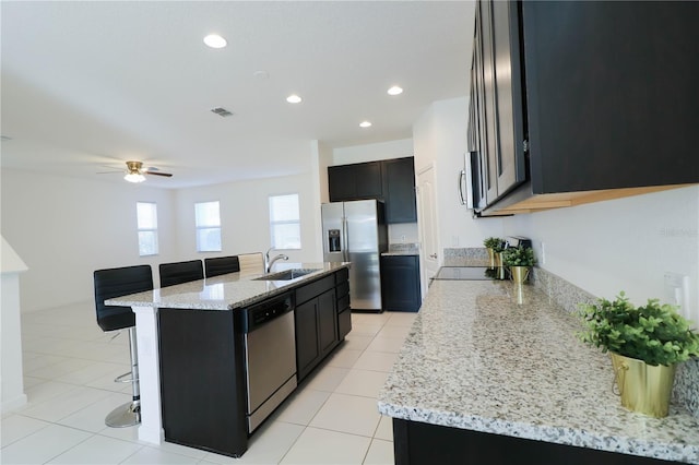 kitchen with stainless steel appliances, a breakfast bar, a sink, light stone countertops, and a kitchen island with sink
