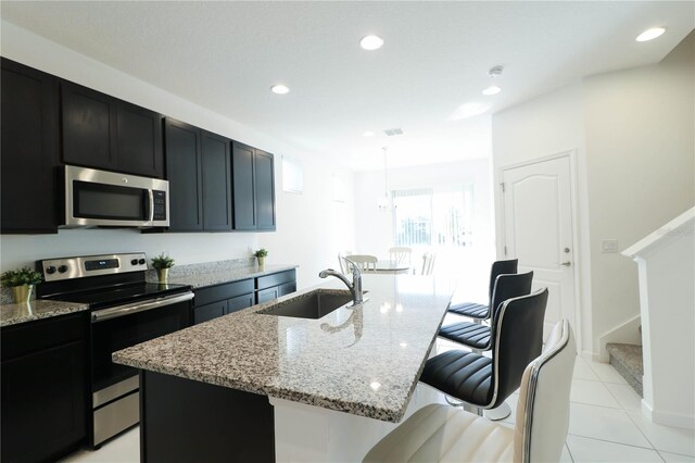 kitchen with light stone counters, a sink, a breakfast bar area, stainless steel appliances, and a center island with sink