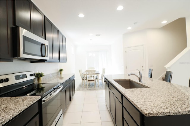 kitchen with recessed lighting, an island with sink, light stone counters, a sink, and appliances with stainless steel finishes