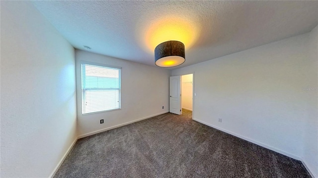 spare room featuring dark colored carpet, baseboards, and a textured ceiling