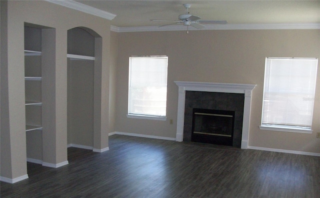 unfurnished living room featuring a tiled fireplace, built in shelves, a ceiling fan, wood finished floors, and ornamental molding