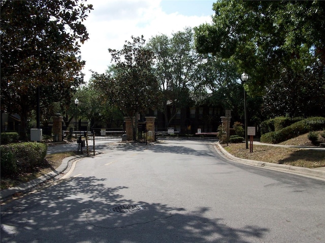 view of road featuring a gate, curbs, street lighting, and a gated entry