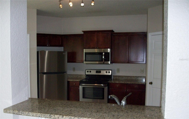 kitchen with dark brown cabinets, a textured wall, light stone countertops, a peninsula, and appliances with stainless steel finishes