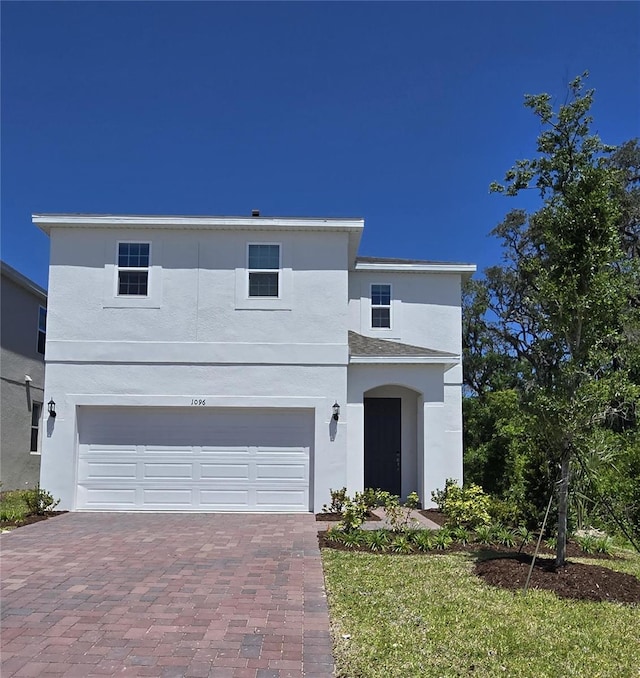 view of front facade with stucco siding, a garage, and decorative driveway