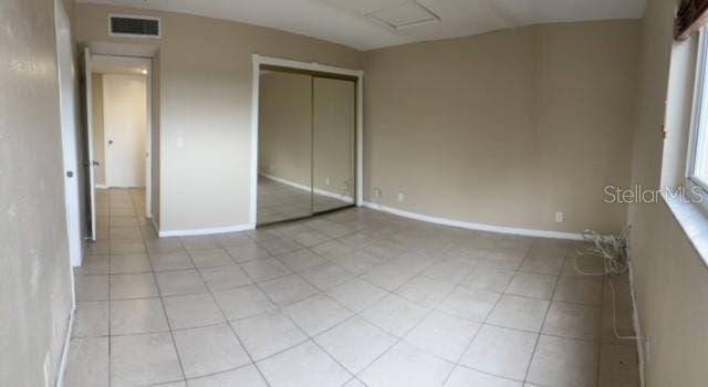 unfurnished bedroom with a closet, attic access, light tile patterned floors, baseboards, and visible vents
