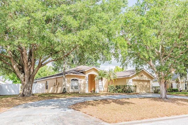 ranch-style home featuring a garage, driveway, fence, and stucco siding